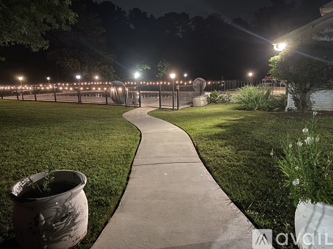 A pathway leads through a grassy area with lights on the fence.