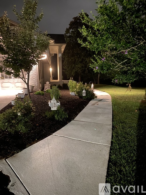 A white house with a lit up porch and a sidewalk in front.
