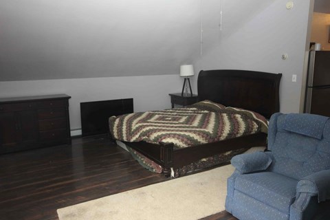 A bedroom with a bed, chair, and nightstand.