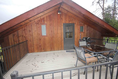 A wooden building with a black door and a table and chairs on a deck.