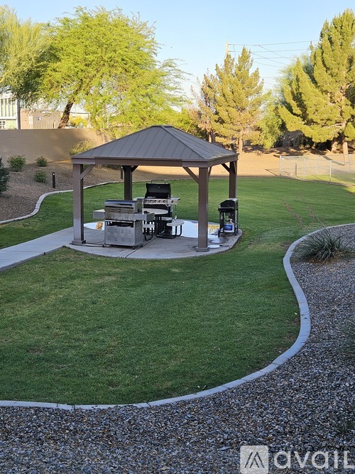 A gazebo with a grill is surrounded by a gravel path in a grassy area.