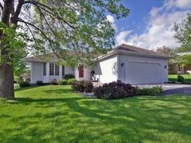A white house with a red door is surrounded by green grass and trees.