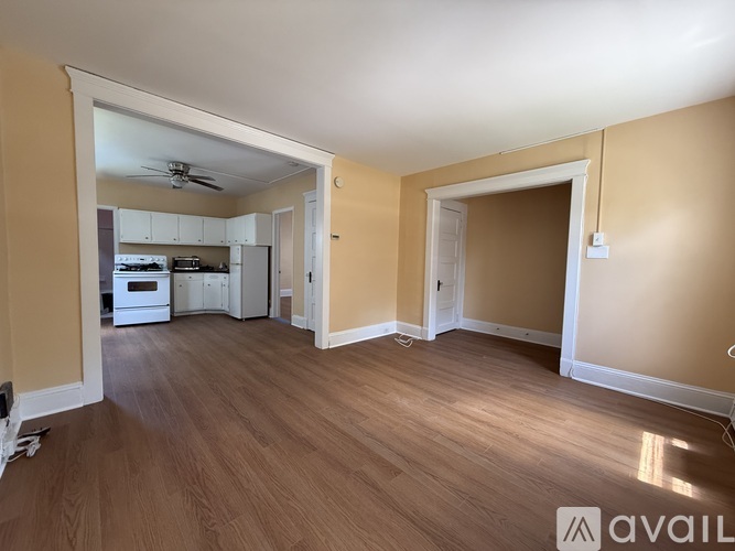 A spacious room with wooden flooring and a kitchen area in the background.