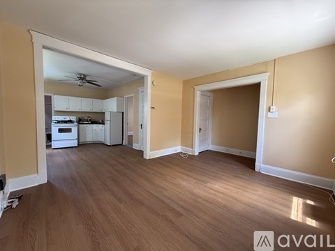 A spacious room with wooden flooring and a kitchen area in the background.
