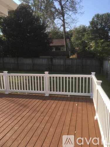 A wooden deck with a white railing and trees in the background.