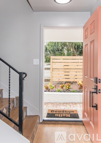 A hallway with a wooden staircase and a red door leading to a garden.