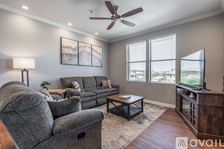 A living room with a grey couch, a grey chair, a wooden coffee table, a ceiling fan, and a painting on the wall.