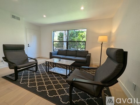 A living room with a black and white patterned rug, a black leather sofa, a black leather chair, and a black leather armchair.