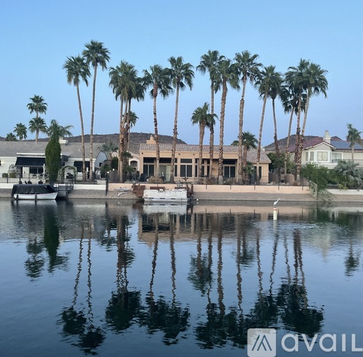 A house is reflected in the water in front of a row of palm trees.