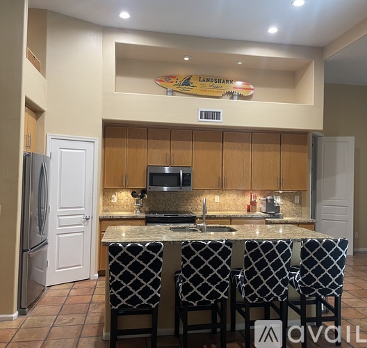 A kitchen with a fridge on the left and a counter with four chairs.