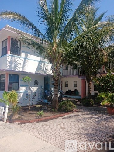 A white building with a red trim and a palm tree in front.