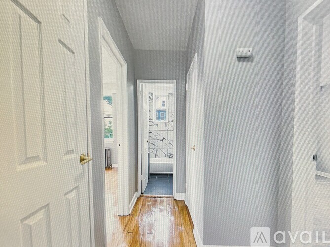 A hallway with a wooden floor and white walls leading to a door.