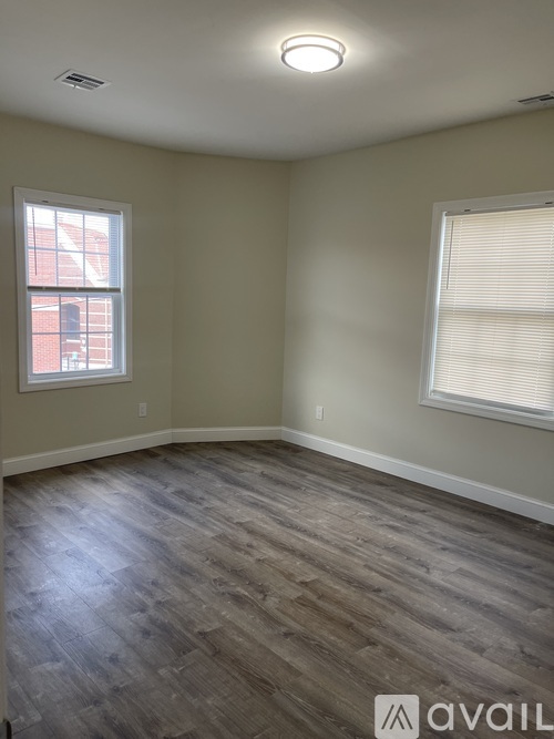 A room with wooden flooring and two windows.