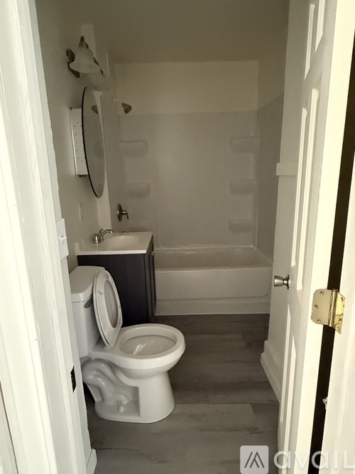 A white toilet is in a small bathroom with a white tub.