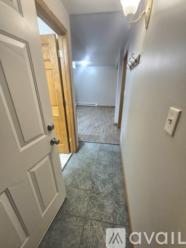 A hallway with a door on the left and a light switch on the wall.