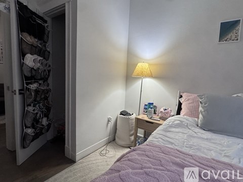 A bedroom with a bed, a nightstand with a lamp, and a closet with shoes.