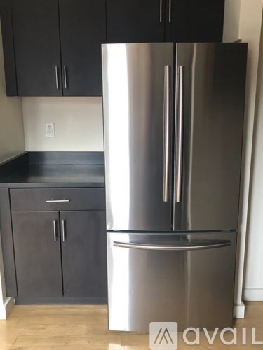 A stainless steel refrigerator stands in a kitchen with black cabinets.