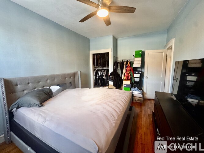 A bedroom with a bed, a ceiling fan, and a closet with clothes hanging.