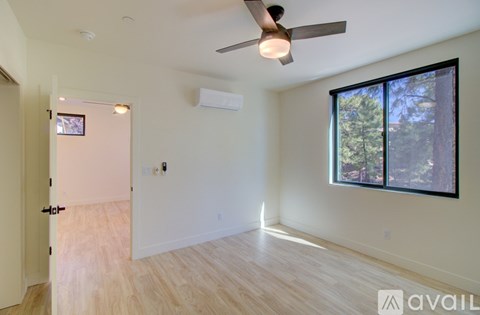 A room with a ceiling fan and a window overlooking trees.