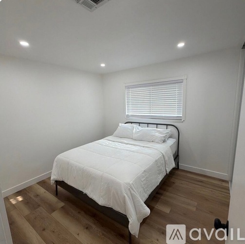 A bedroom with a bed, wooden floor, and a window with blinds.