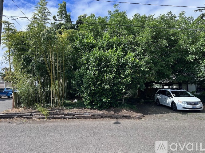 A white car is parked in front of a house with a tree in front of it.