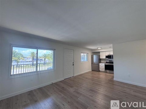 A spacious living room with hardwood floors and a view of a balcony with palm trees.