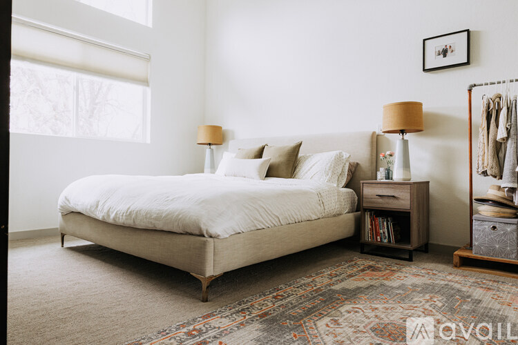 A bedroom with a large bed, a nightstand with a lamp, and a clothing rack.