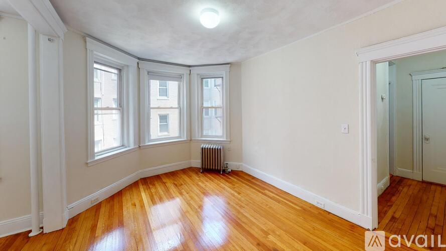 A room with wooden floors and white walls has a window with a view of a building outside.