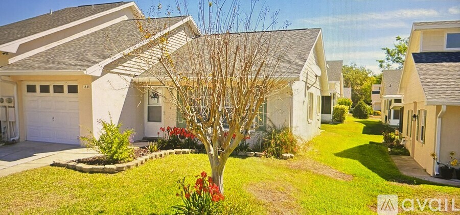 A tree with red flowers is in the front yard of a house.