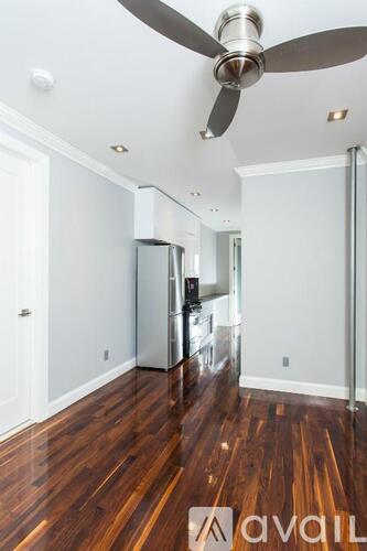 A kitchen with a refrigerator, wooden floors, and a ceiling fan.