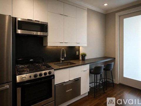 A modern kitchen with a stainless steel refrigerator and oven, white cabinets, and a dark countertop.