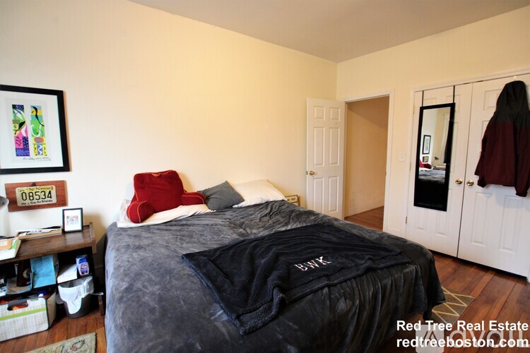 A bedroom with a bed covered in a black comforter and a red pillow.