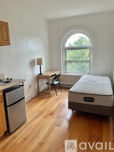 A small room with a mattress, a table, a chair, a fridge, and a stove.