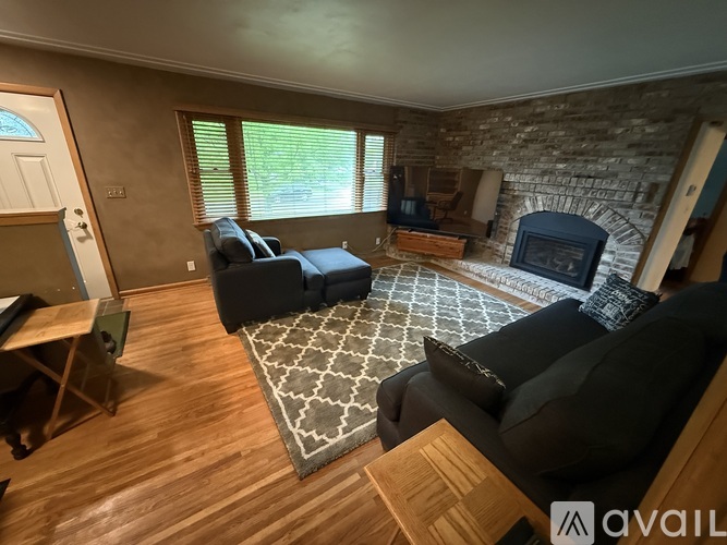 A living room with a stone fireplace and a grey rug.