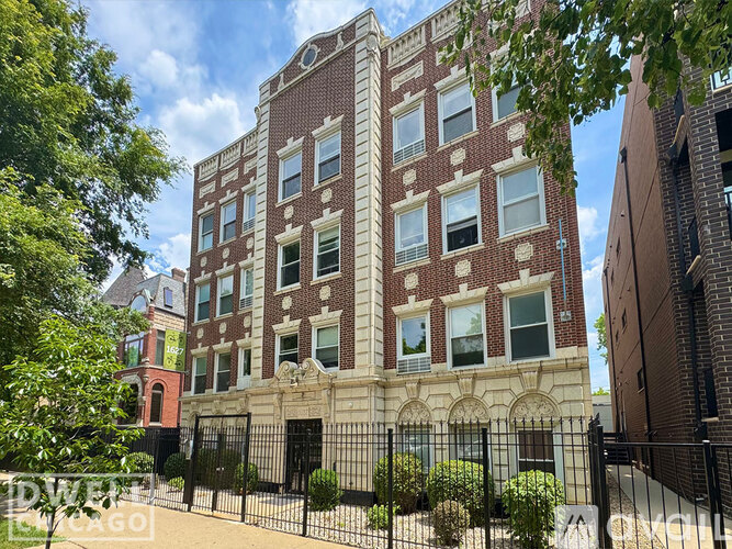 A red brick building with a black fence in front.