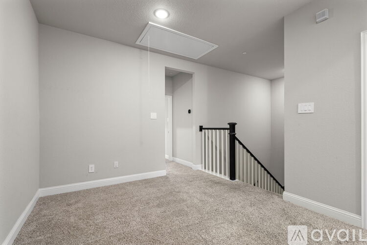 A spacious room with a carpeted floor and a staircase with a black railing.