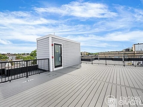 A small white building with a red fire alarm on the side is situated on a wooden deck.