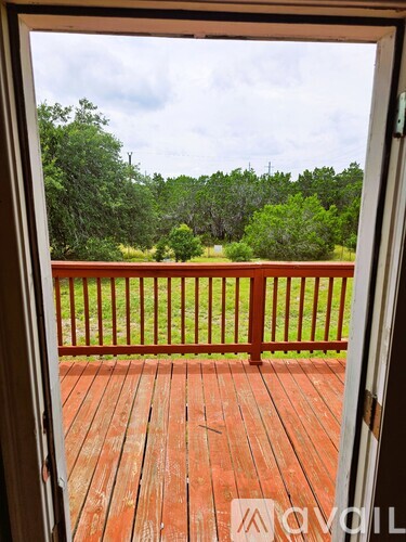 A wooden deck with a view of a green lawn and trees.