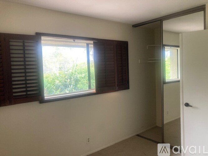 A room with a window covered by wooden shutters and a door leading to another room.