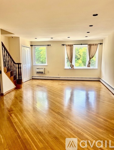 A spacious room with wooden floors and a staircase on the left side.