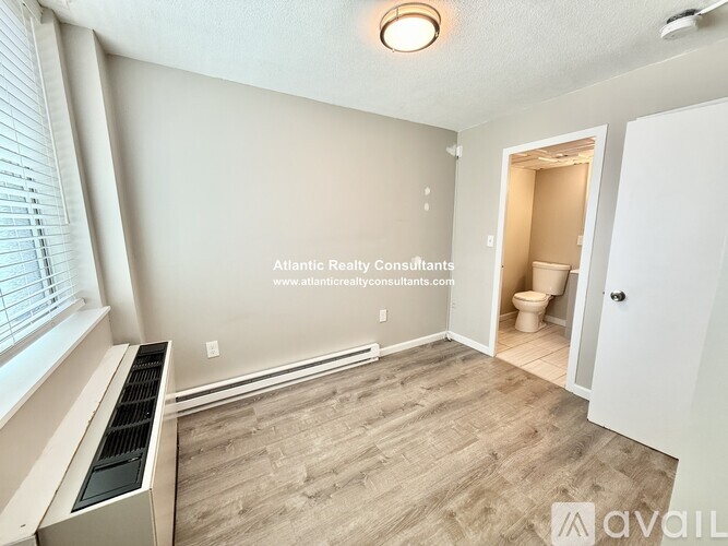 A room with a window, a heater, and a door leading to a bathroom.