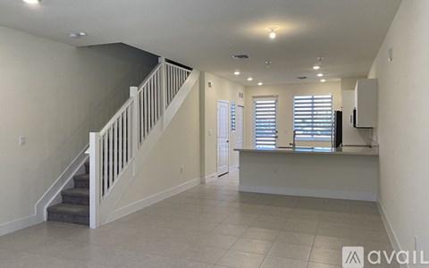 A spacious room with a staircase and a window with blinds.
