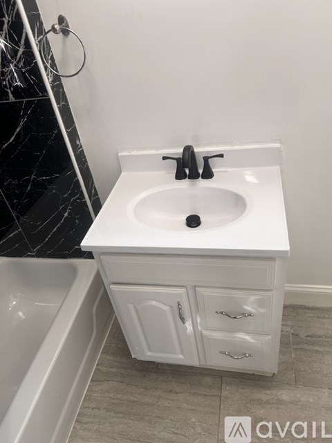 A white sink with a black faucet is in a bathroom with a white cabinet and a white bathtub.