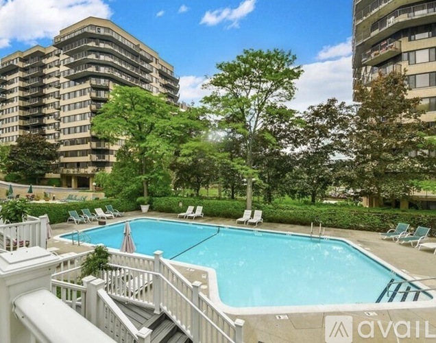 A pool surrounded by trees and chairs with apartment buildings in the background.
