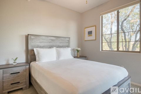 A bedroom with a large bed, a nightstand with a plant, and a framed picture on the wall.