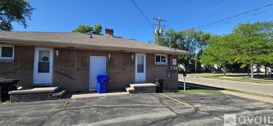 A small house with a white door and a blue trash can in front.