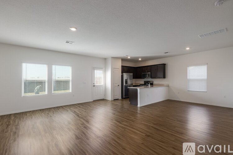 A spacious living room with wooden flooring and a kitchen area in the background.