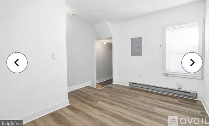 A room with wooden flooring and white walls, with a window on the right side.