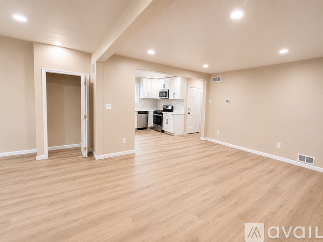 A spacious room with wooden flooring and a kitchenette in the background.