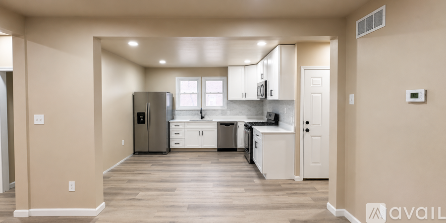 A kitchen with white cabinets and a refrigerator in a room with wooden floors.